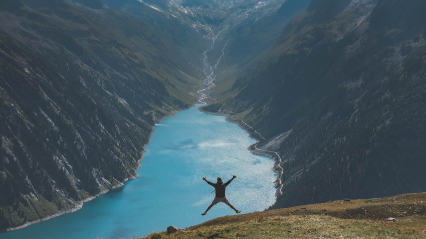 A person jumping in the air looking down over a lake in a vast valley
