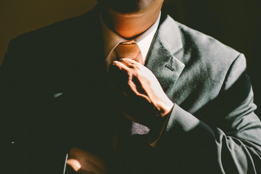 A gentleman wearing a black suit fixing his tie